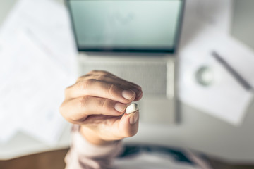 Top view. Tired business woman  holding a headache pill on the workplace with glass of water on the background of graphics and charts printed on the paper.