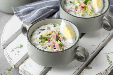 Traditional cold Russian soup okroshka, with sausage (ham), potatoes, boiled egg, fresh vegetables (cucumber, radish), green onions and dill. Yogurt, kefir, mineral water