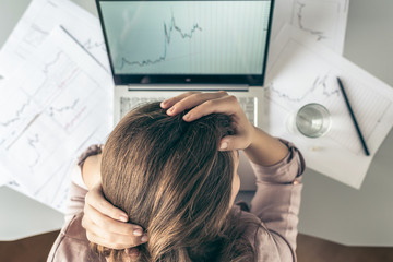 Top view. Tired business woman with headache at office with glass of water and pill on the background of graphics and charts printed on the paper. 