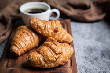 Breakfast with fresh croissants and cup of black coffee on wooden board
