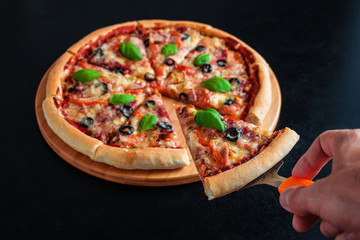 man hand holding slice of homemade pizza with spatula on black background