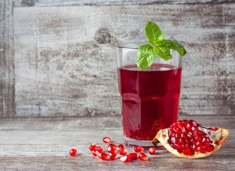 A glass of pomegranate juice with fresh pomegranate fruits on wooden table. Vitamins and minerals. Healthy drink concept.