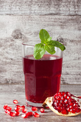 A glass of pomegranate juice with fresh pomegranate fruits on wooden table. Vitamins and minerals. Healthy drink concept.