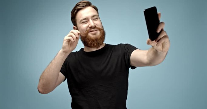 handsome ginger haired hipster man with mustache and beard taking a selfie and sending it with his smart phone device. slow motion 4K shot.