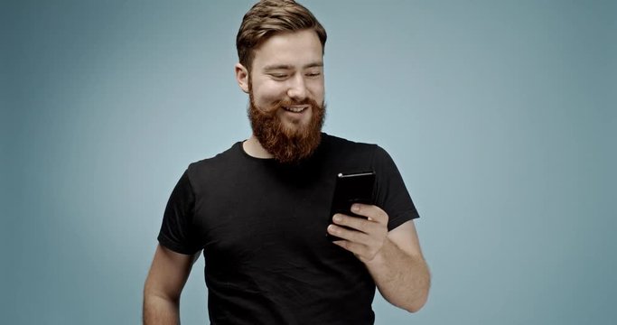 handsome ginger haired caucasian young hipster man with mustache and beard texting with his girlfriend and taking a selfie and sending it with his smart phone device. slow motion 4K shot.
