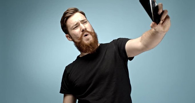 caucasian young hipster man with ginger mustache and beard texting with his girlfriend, taking a selfie and sending it with his smart phone device. slow motion 4K shot.