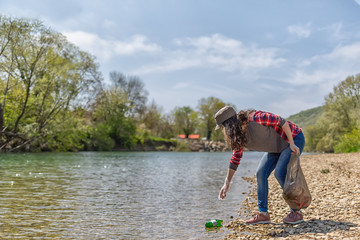 A young woman volunteer collects garbage along the river. The concept of earth day and ecology and...