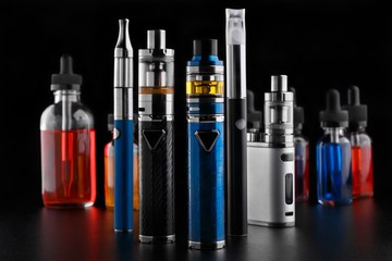 Electronic cigarettes and bottles with vape liquid on black background