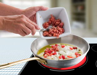 Sofrito de boloñesa, mano poniendo carne sobre sartén al fuego. Bolognese stir-fry, hand putting meat on pan over fire.
