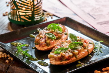Bruschetta with vegetables and basil on a black square plate on a wooden background. close-up