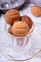 Walnut shaped cookies with caramel in a glass cup on the white table. Special skillet in the background