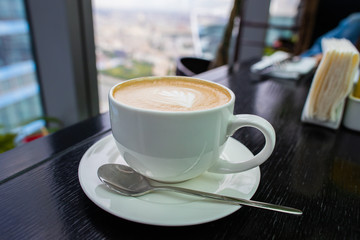 white Cup of cappuccino coffee with foam on the table in a cafe or restaurant with a shiny spoon