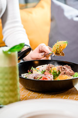 green smoothie and salad with avocado, tomatoes, poached egg, beef, orange, onion and arugula in a black plate on a table in a restaurant. girl eating salad in a restaurant. close up
