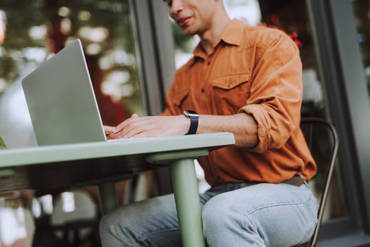 Young man in orange shirt using laptop outdoors