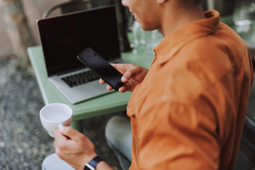 Young man drinking coffee and using cellphone in outdoor cafe