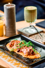 Roasted meat on pumpkin puree with sprouts on a black plate on a table in a restaurant. Matcha latte and candles on background. Close up. Space.