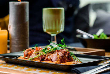 Roasted meat on pumpkin puree with sprouts on a black plate on a table in a restaurant. Matcha latte and candles on background. Close up. Space.