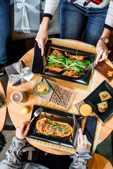 Two girls have breakfast in the restaurant. Spring rolls and grilled meat with pumpkin puree on black plates on a light wooden table in a restaurant. Flat lay. top view