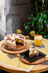 Beautiful chocolate layered cake with yellow filling and beautiful coffee glaze, decorated with tubules and pastry beads. Cake on a beautiful yellow background on a wooden table in the restaurant