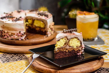 Beautiful chocolate layered cake with yellow filling and beautiful coffee glaze, decorated with tubules and pastry beads. Cake on a beautiful yellow background on a wooden table in the restaurant