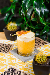 Yellow cocktail with white protein foam in a beautiful old fashion glass, decorated with a mango skewer, on a yellow background. Close-up