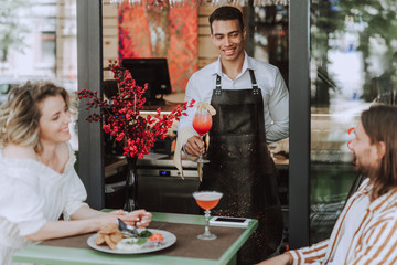 Handsome bartender serving cocktail to young couple