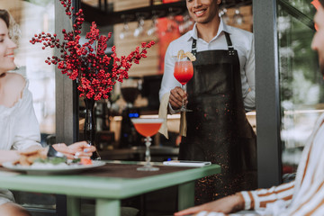 Handsome bartender serving cocktail to visitors in outdoor cafe