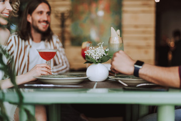 Young people sitting at the table with beautiful flower and cocktails