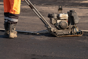 Road workers compact the asphalt with a vibrating rammer on the road. Worker with compactor at a road construction site