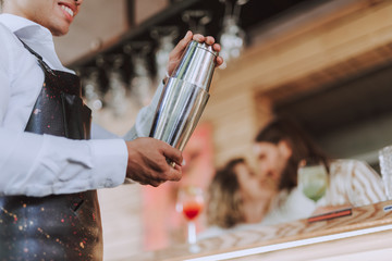 Smiling bartender with shaker preparing cocktail at bar