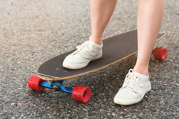 Close-up of female legs in rag sneakers on a longboard on the background of asphalt at sunset. Big skateboard with girl legs. Youth leisure concept