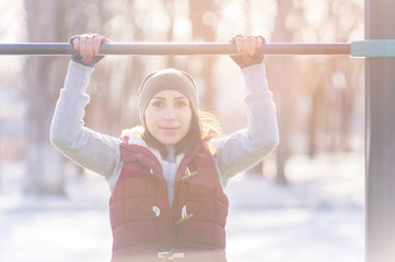 Attractive girl involved in sports workout on a horizontal bar on a sunny winter day. The concept of sports activities all year round