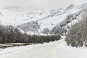 Empty mountain asphalt road in winter covered with snow on a cloudy day. The concept of driving a car in winter ice and travel