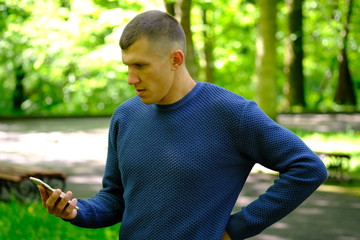 Young stylish man stay in a park and holding mobile phone. Lifestyle Outdoor street photo