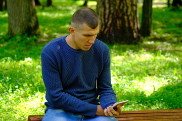 Young man sitting on a bench in a park and holding mobile phone. Lifestyle Outdoor street photo