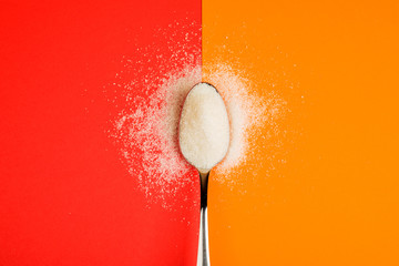 sugar with spoon on red and yellow background - obrazy, fototapety, plakaty