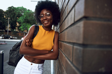 Smiling young afro-american woman leaning on brick wall in the city