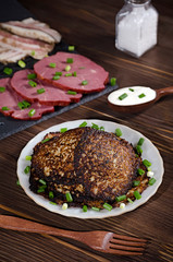 potato pancakes with green onions and sour cream on a dark wooden table, sliced pork and bacon