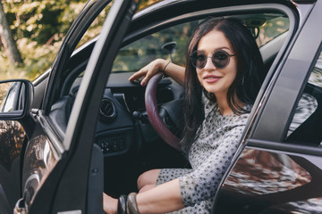 Obraz na płótnie Canvas smiling pretty stylish brunette woman with sunglasses in car opens or closes the door