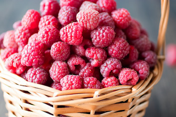 Fresh raspberries in brown basket on gray background.