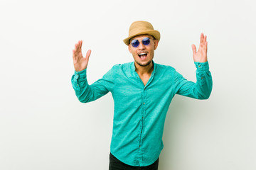 Young hispanic man wearing a summer clothes receiving a pleasant surprise, excited and raising hands.