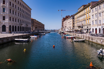 Fototapeta na wymiar Grand Canal of Trieste with turquoise waters reflecting the buildings, with boats on both banks and in the background the Adriatic Sea, Trieste, Italy