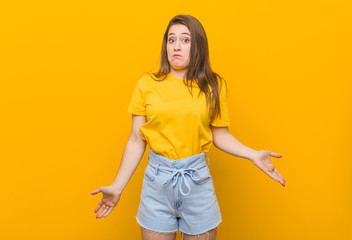 Young woman teenager wearing a yellow shirt shrugs shoulders and open eyes confused.