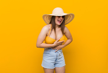 Young caucasian woman wearing a straw hat, summer look laughs happily and has fun keeping hands on stomach.
