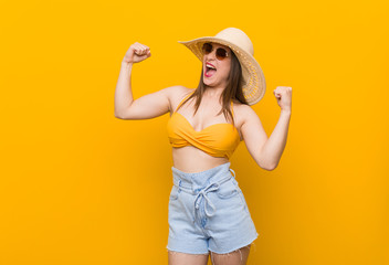 Young caucasian woman wearing a straw hat, summer look raising fist after a victory, winner concept.