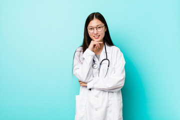 Young chinese doctor woman smiling happy and confident, touching chin with hand.