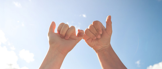 Two hands of friends and friendship symbol on blue sky background