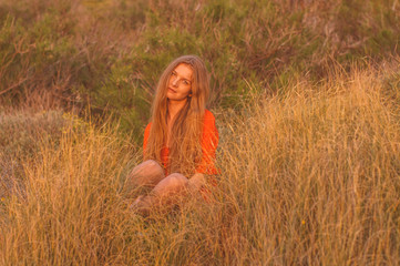 Young blonde girl in red dress sitting on grass