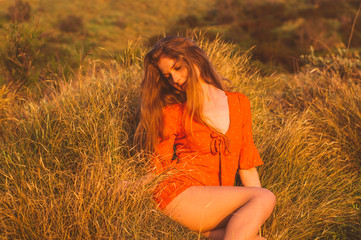 Young blonde girl in red dress sitting on grass