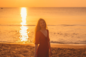 Young blonde girl in red dress staying in the evening on the beach